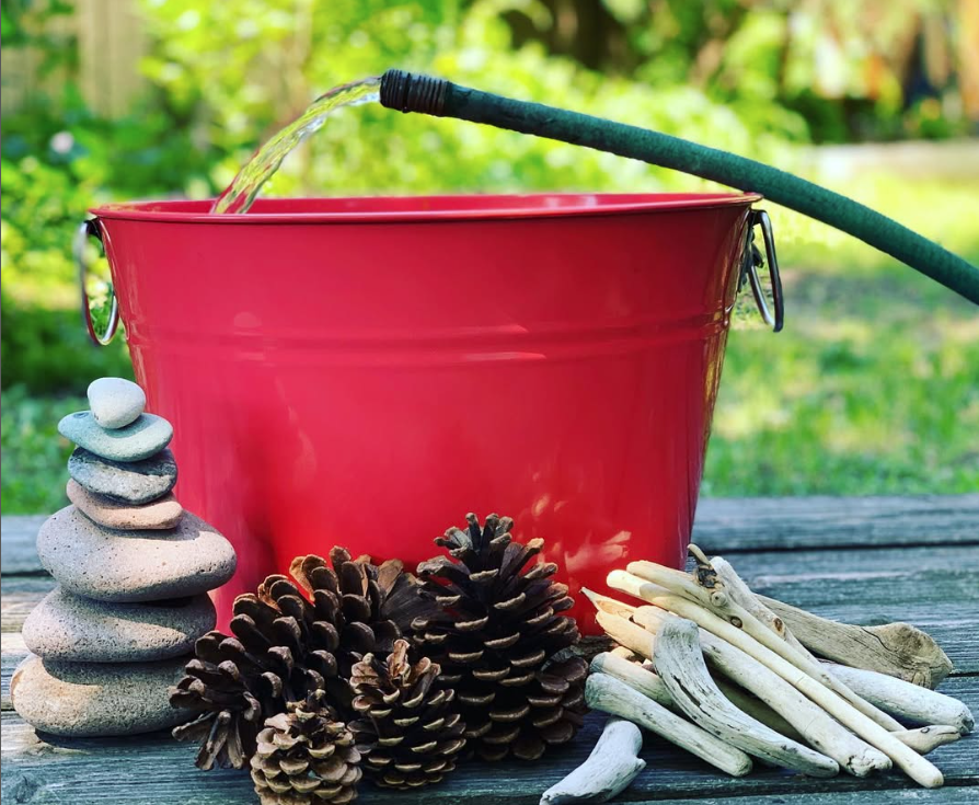 red bucket next to stack of rocks, pinecones, twigs